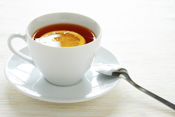 A cup of tea with a slice of lemon with a white flare on the surface. Simple content.