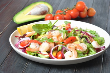 Avocado salad with shrimps, cherry tomatoes, arugula beet leaves, red onion, yellow sweet pepper. Healthy lunch plate with vegetables and shrimps