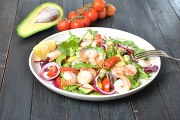 Avocado salad with shrimps, cherry tomatoes, arugula beet leaves, red onion, yellow sweet pepper. Healthy lunch plate with vegetables and shrimps