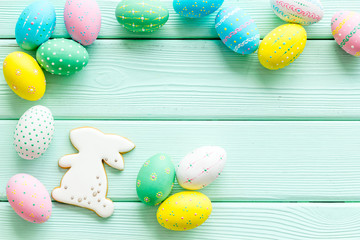 Easter symbols. Painted eggs and bunny gingerbread on green wooden desk top-down frame copy space