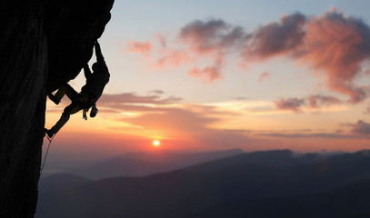 Male climber in rock climbing equipment, pulling up and doing next step on high cliff reaching rocky top. Side view. Panoramic view of mountains and amazing pink sky with sunset and clouds. Copy space - obrazy, fototapety, plakaty