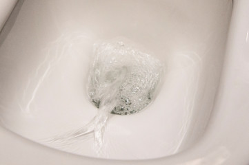Water drains in a white toilet close-up. Plumbing Design