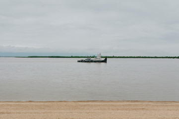Obraz premium river ferry sails on a calm river, the sandy shore of a gray river in gloomy weather