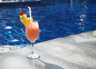  Glass glass, on a thin leg, with an orange drink with ice, on the edge of the pool, with pieces of pineapple, yellow, decorated with red cherry, with transparent tubes, for a holiday in the hotel 
