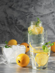 One glass with lemonade or mojito cocktail with lemon and mint and cup with ice. Cold refreshing drink or beverage with ice on dark background. Copy space