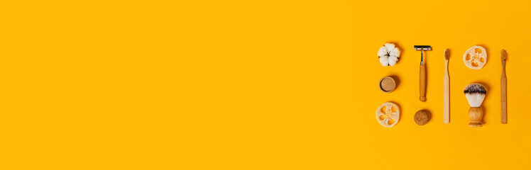 Zero waste web banner. Natural bamboo toothbrushes, razor, cap of paper tube, natural sponge, shaving brush, rag bag, cotton flower and natural soap on yellow background. Flat lay, top view.