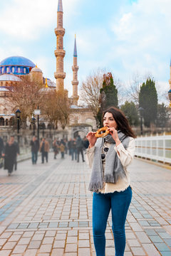 Beautiful woman tourist eats traditional street food Simit or Bagel in English with view of Sultanahmet Mosque or Blue Mosque,a popular destination in Istanbul,Turkey