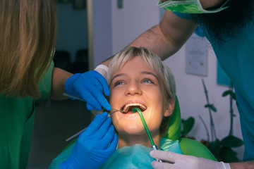 Dentist in green uniform examining the teeth of a beautiful female patient