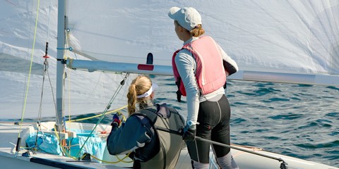 Children Sailing small sailboat with a on an inland waterway.