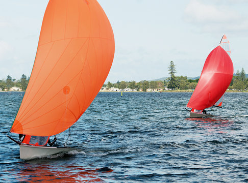 Children Sailing small sailboat with colourful orange and red sails on an inland lake.