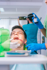 Closeup picture of a female dentist examining teenage boy's teeth in the dental office.