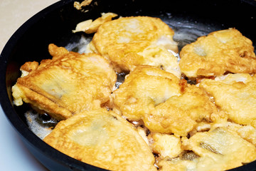 Fried fish in batter hisses in a hot pan. Ethnic regional food. Background and texture of food