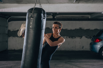 Young sportswoman doing high kick during boxing exercise in a garage.