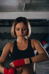Closeup portrait of a beautiful woman doing red boxing bandages in a garage.