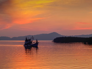 Sea view evening of fishing boat running in the sea with red sun light and cloudy sky background, twilight at Kuraburi Pier, Phang Nga, southern of Thailand.