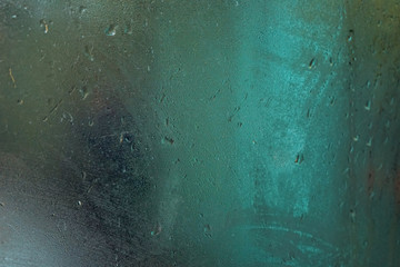 Wet steamy window inside bus on a rainy day, blurred green neon light background