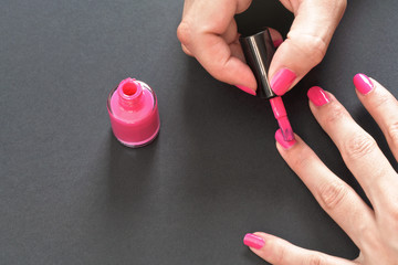 Applying pink nail polish - closeup photo of woman hands, little brush over fingernails, small bottle on gray / black background