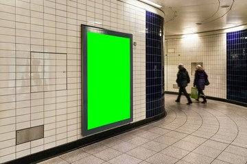 Advertising board display green mockup on wall with white tiles at underground station passage, blurred people in background