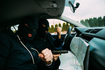 Bank robbers with their masks on pointing at the map prepared for robbing the bank,sitting in the car and waiting for the right time to rob.