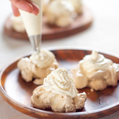 the process of creating Pavlova dessert, decorating the meringue with cream from the culinary bag