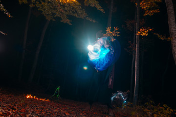 Sorcerer (magician) casting a spell while standing in the magical woods. Holding his magical staff. Magic illumination. Autumn holiday celebration. Mystery and nightmare concept.
