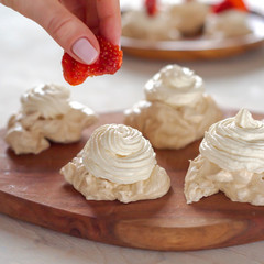 the process of creating Pavlova dessert, decorating the meringue with strawberries