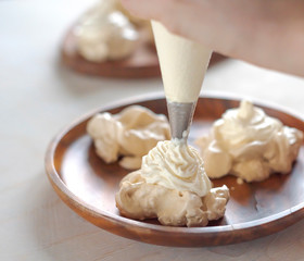 the process of creating Pavlova dessert, decorating the meringue with cream from the culinary bag