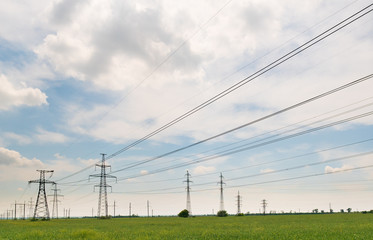 Obraz premium High-voltage power lines passing through a green field, on the background of a beautiful cloudy sky