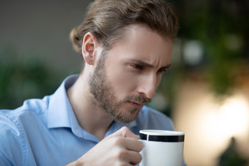 Young serious man with smart look with cup in his hand.
