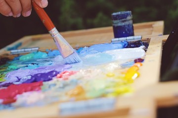Close up mixing oil paints on the palette. Colorful workplace of the artist with oil paints. Oil paints texture background.