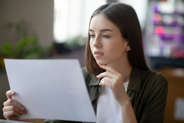 Attentive smart girl looking at a paper sheet in hand.