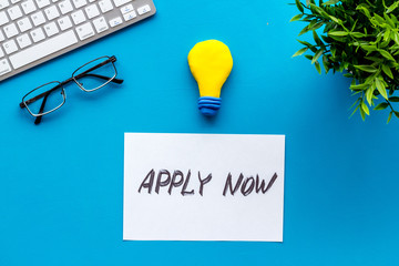 Apply now. Text on blue office desk top-down