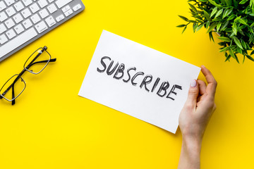 Subscribe. Advertisement in hand on yellow office desk top-down