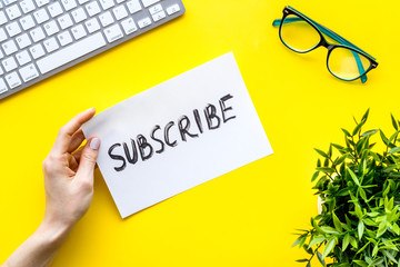 Subscribe. Advertisement in hand on yellow office desk top-down