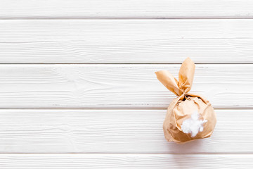 Easter gift in shape of bunny with tail on white wooden background top-down copy space