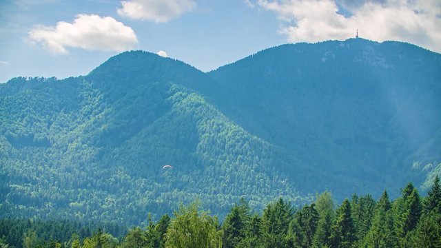 Paraglider flies in hilly landscape with high pick Urslja Gora, Kotlje, Slovenia