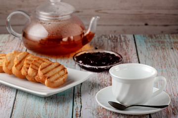 Freshly made tea in a teapot with cookies and jam on the table