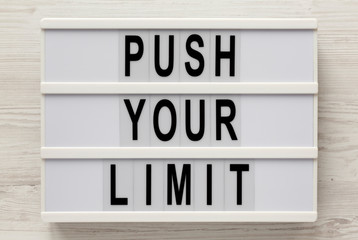 'Push your limit' words on a lightbox on a white wooden background, top view. Overhead, from above, flat lay. Close-up.