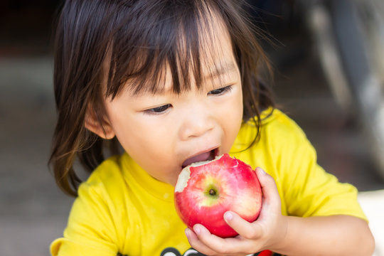 Portrait image of 1-2 years old of baby. Happy Asian child girl eating and biting an red apple. Enjoy eating moment. Healthy food and kid concept.