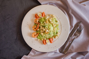 Cesar salad with shrimps on the grey table with towel decor.
