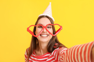 Woman in funny disguise taking selfie on color background. April fools' day celebration