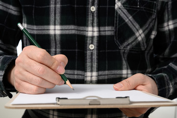 A close-up of a man's hand signing a document with a clipboard