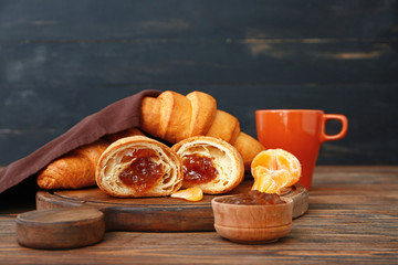 Board with tasty sweet croissants and jam on wooden table