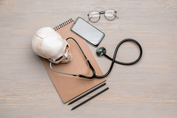 Stethoscope with human skull, notebook and mobile phone on wooden table