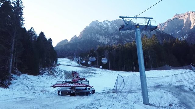 Partially snow covered ski slope near Busteni city , Prahova Valley , Romania, with he Carpathian mountain ridge behind , functional ski lift installation and snow grooming machine.