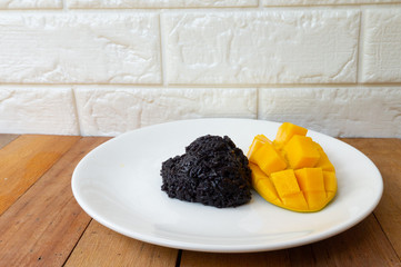 Black sticky rice and golden yellow mango put on a white plate placed on a wooden table.