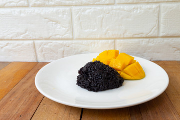 Black sticky rice and golden yellow mango put on a white plate placed on a wooden table.
