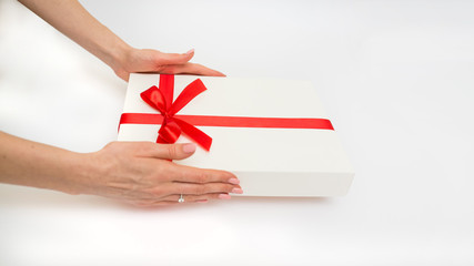 Female hands holding a gift box white with a red ribbon