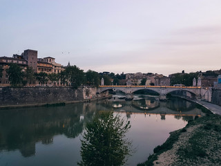 Fototapeta na wymiar Beautiful river scene in Rome with a bridge and houses at early evening. 