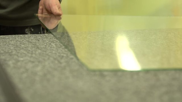 Worker cutting glass panel with a ruler and knife. Shortening glass sheet with hands. Cutting off a small piece of a big glass panel on a working table. Clean simple cut in the glass.